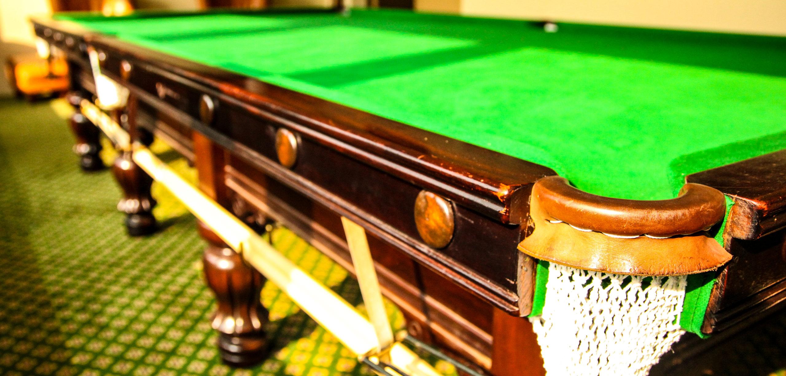 Snookertisch im Detail: Mahagoni-Bande und Ledertasche auf gemustertem Teppich