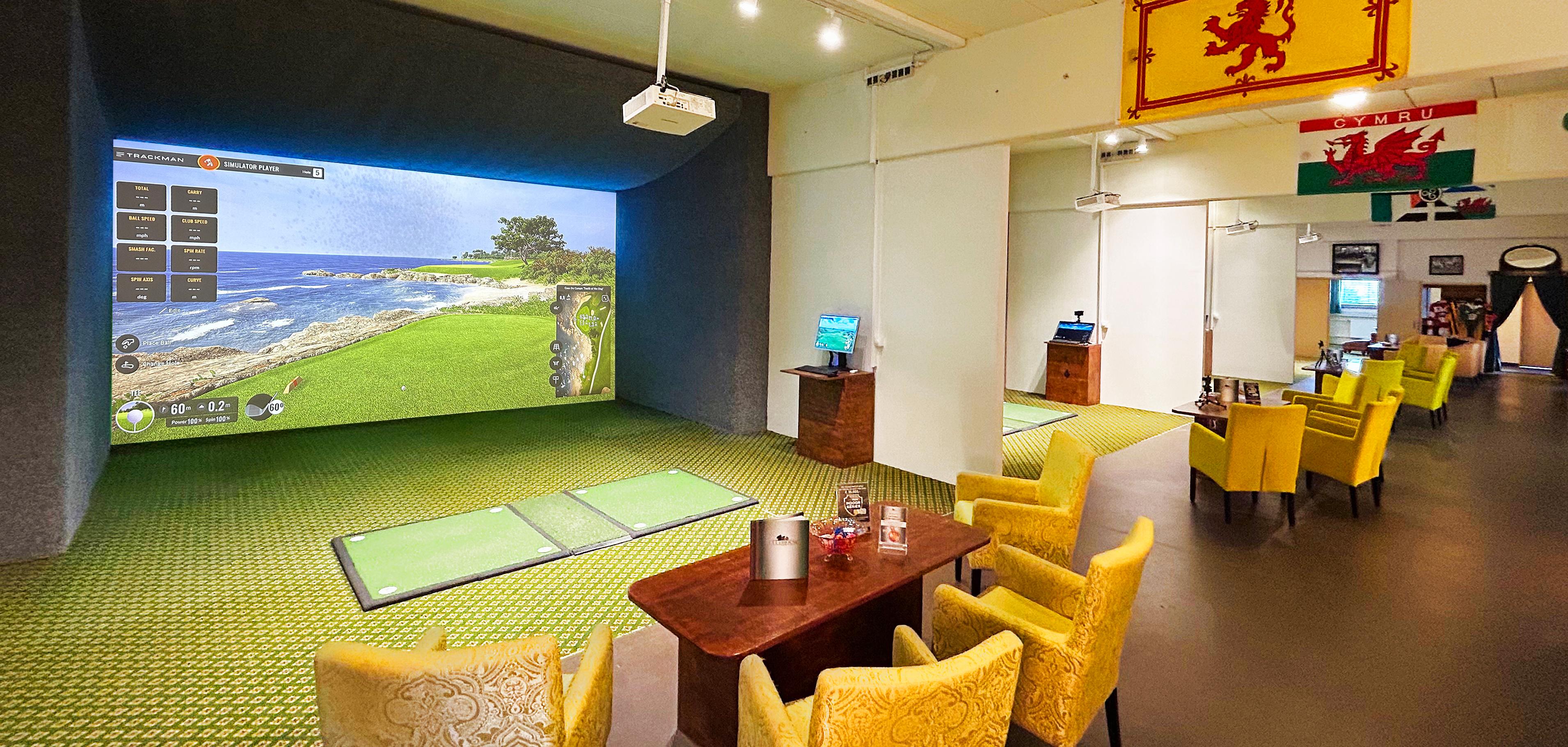 Simulator-Abschlag mit Pebble Beach auf der Trackman-Leinwand, gelbe Paisley-Sessel, schottische und walisische Flagge