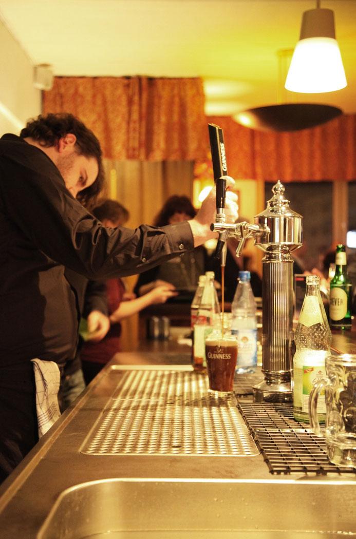 Barkeeper zapft ein Guinness, Gäste unscharf im Hintergrund